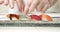Closeup male hands of cook in gloves putting sashimi with salmon, tuna and shrimp on a plate.