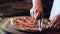 Closeup of male hands cuting pizza with round knife