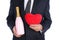 Closeup of a man in a gray business suit holding a pink bottle of sparkling wine and a red plush heart in front of his torso, man