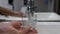 Closeup of a man hand holding a glass pour filtered drinking water. The person consumes water. Fill a glass with tap water
