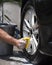 Closeup man hand washing new car alloy silver wheels with big scrub brush, soap suds and bucket