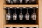 Closeup many upside down empty clear transparent crystal upturned wine glasses hanging in straight row on brown wooden shelf, rack