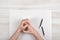 Closeup masculine folded hands on wooden panel with white paper and broken black pencil in top view.