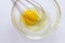 Closeup of metal whisk and chicken yolk in a glass bowl