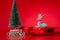 Closeup of a miniature decorative reindeer on a sleigh next to a Christmas tree on a red background