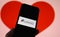 Closeup of mobile phone screen with logo lettering of online dating agency app lovoo, blurred heart background