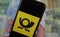 Closeup of mobile phone with yellow black Deutsche Post logo, blurred euro money paper currency background