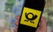 Closeup of mobile phone with yellow black Deutsche Post logo, blurred euro money paper currency background