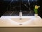 Closeup of modern bathroom pure white washbasin with chrome faucet and vase with flowers. wall made of black marble