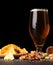 Closeup of moist glass of brown ale, with crisps, bacon, peanuts, hazelnuts, and pistachios on a dark background. Snacks