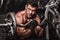 Closeup of a muscular young man lifting weights on dark background