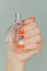 Closeup nail polished multicolored nails hand holding perfume bottle