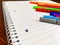 Closeup of notebook spiral and colorful pens laying on an empty white notebook with lines, used for note taking in school, while