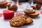 Closeup oatmeal cookies, burning candles, cones, dry leaves and two glasses on a wooden white table.