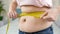 Closeup of obese woman measuring her big belly with yellow measuring tape. Concept of dieting, unhealthy lifestyle