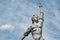 Closeup of old dilapidated stone statue of Soviet woman with rising hand on sky background.