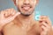 Closeup of one smiling mixed race man flossing his teeth against a blue studio background. Guy holding container of