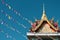 Closeup of an ornate Buddhist temple roof with colorful banners against a clear blue sky