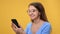 Closeup overjoyed woman in eyeglasses chatting smartphone having good news isolated on orange studio