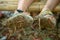 Closeup of pair of dirty sandals full of mud and hay worn by a boy sitting on a bamboo bench.