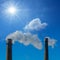 Closeup pair of industrial pipes with smoke on blue sunny sky background