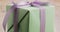 Closeup pan of green gift box with purple ribbon bow on old wood table