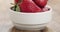 Closeup pan of ripe organic strawberries in white bowl on wood table
