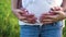 Closeup of parents hands touching pregnant belly in nature