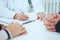 Closeup of patients hands and doctor taking notes.