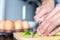 Closeup of people hand and knife slice spring onion on wood butcher and fresh chicken egg in bowl and group of egg in box on