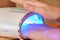 Closeup of a person drying shellac in a LED nail lamp on the table