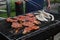 Closeup of a person grilling sausages and meat on an outdoor grill in a park