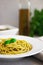 Closeup on pesto pasta in a white plate and in the background a bottle of olive oil. Vertical orientation
