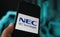 Closeup of phone screen with logo lettering of nec corporation, blurred power circuit background