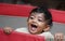 A closeup phot of an adorable indian toddler baby boy smiling with dimple in cheeks and standing inside a playpen.