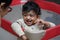 A closeup photo of an adorable indian toddler baby boy smiling with dimple in cheeks at his parent and standing inside a playpen