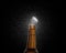 Closeup photo of an amber beer bottle splashing beer drops on a black background. Beer cap flying on top of the bottle