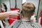 Closeup photo of a barber`s hair clipping a client`s fair hair with a clipper. Male hairdresser creates a stylish hairstyle with