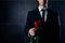 Closeup photo of handsome young man in formalwear holding red rose