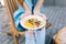 Closeup photo of healthy breakfast in hands of young girl sitting in chair. She wears jeans, blue T-shirt, blue nai