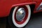 Closeup photo of the rear wheel of a magnificent retro car. The wheel has a red stamped disc in the body color, a large chrome