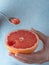 Closeup, photo of a woman holding half of fresh ripe red grapefruit in her hand. Spoon with a slice of grapefruit in hand. Blue