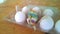 A closeup photograph of a single painted plastic Easter egg nested inside of a plastic egg carton with several real chicken eggs