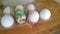 A closeup photograph of a single painted plastic Easter egg nested inside of a plastic egg carton with several real chicken eggs