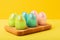 Closeup photography of the glossy easter eggs in the wooden tray on the trendy isometric yellow background.Creative greeting card