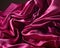 A closeup picture of a piece of magenta satin fabric creased and ruffled in multiple folds. Trendy color of 2023 Viva