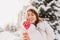 Closeup pink heart lollypop in hands winter girl background chilling on street full with snow in sunny morning. White