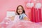 Closeup pink present giving little joyful girl to camera on pink background. Smiling suround big giftboxes, balloons