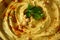 Closeup of a plate of hummus sprinkled with paprika and green leaves of parsley on a blurred gray wooden background.