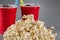 Closeup popcorn on the background of red plastic cups with fizzy drink.